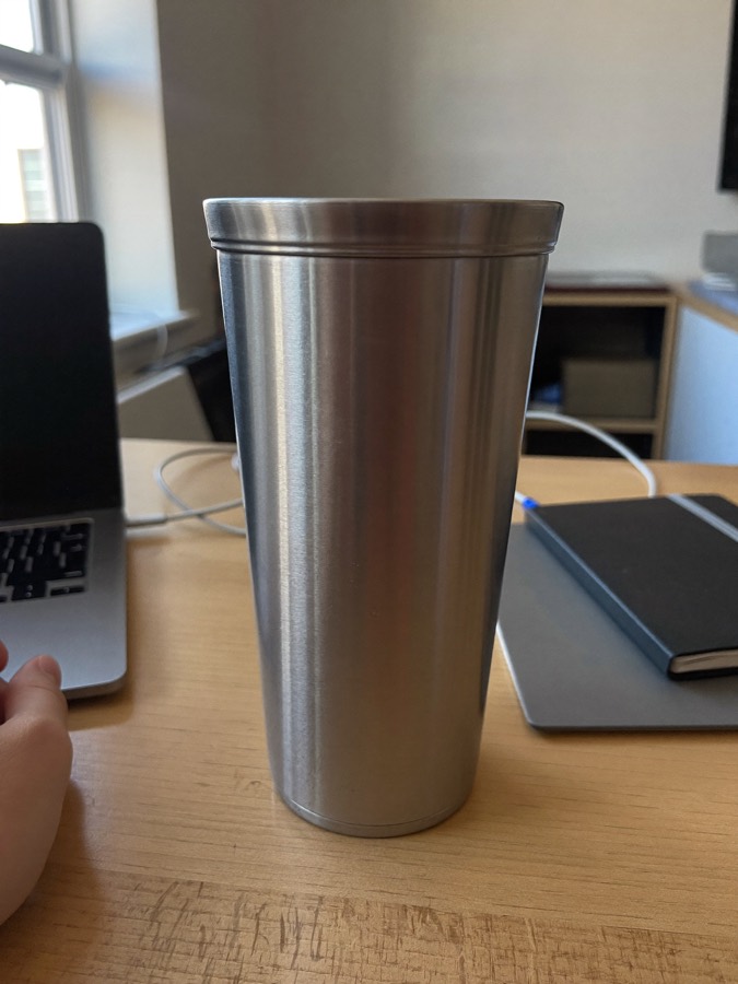 Illustration: a plain steel cup on a coworking desk beside a laptop and a notebook.